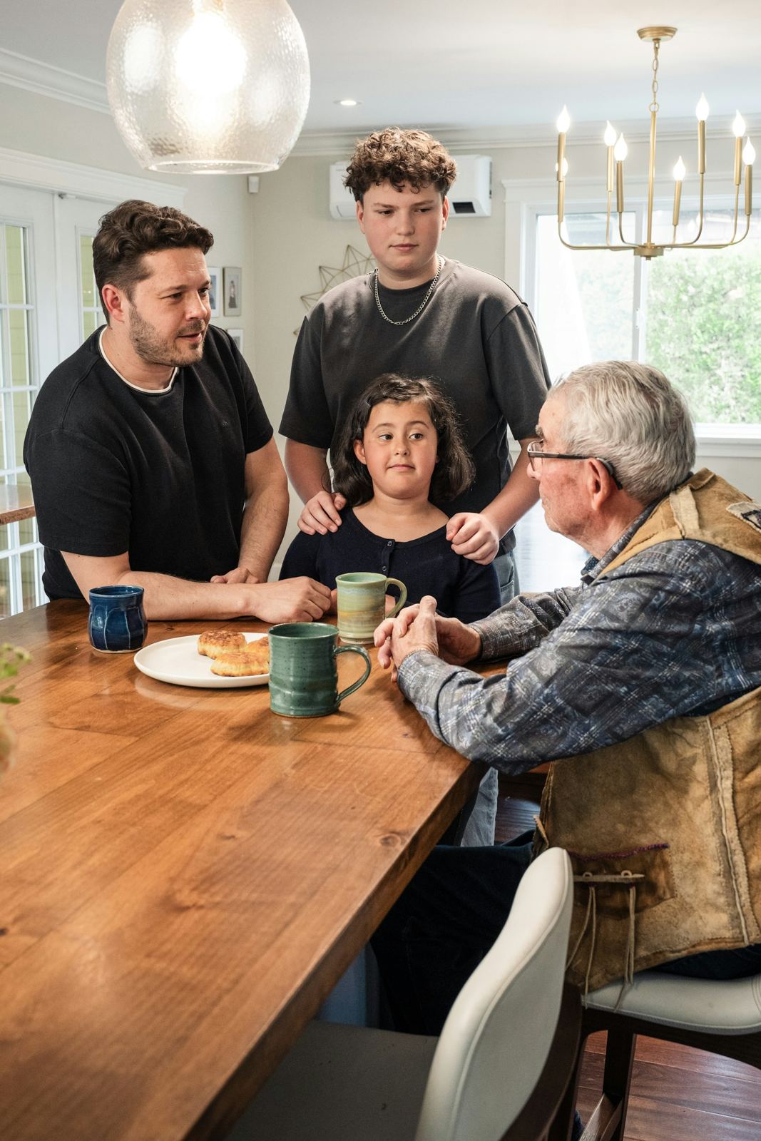 A family gathered around a wooden table with mugs, talking together