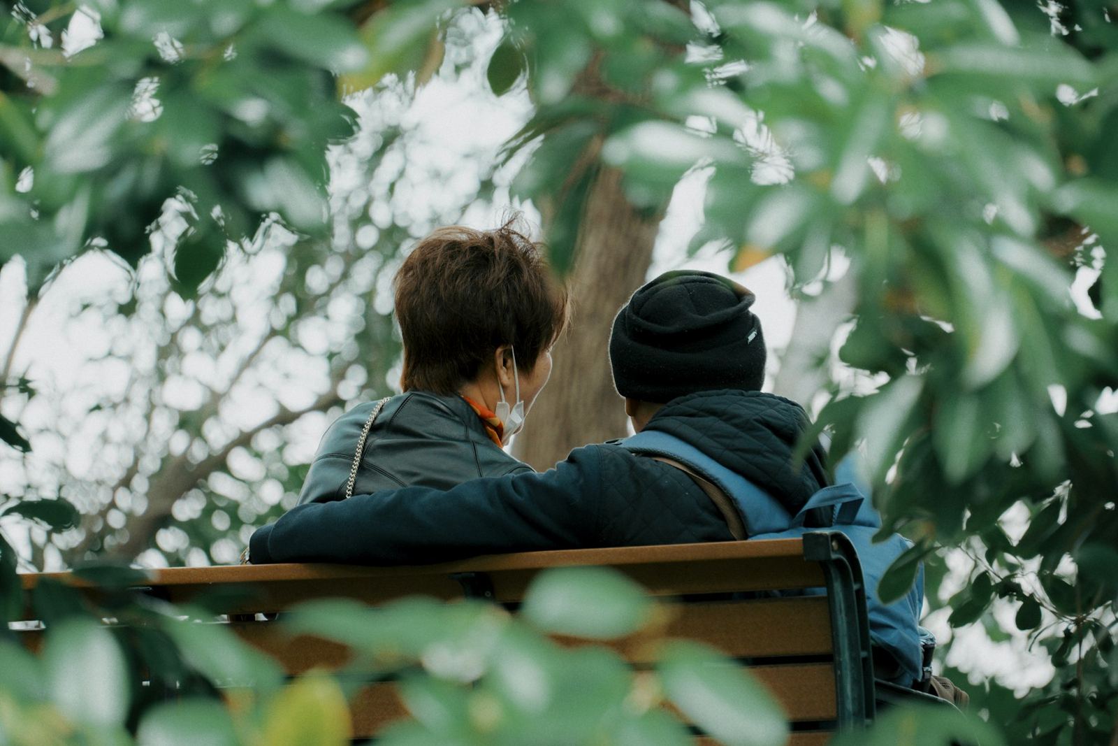 Two people sitting together on a park bench among autumn leaves