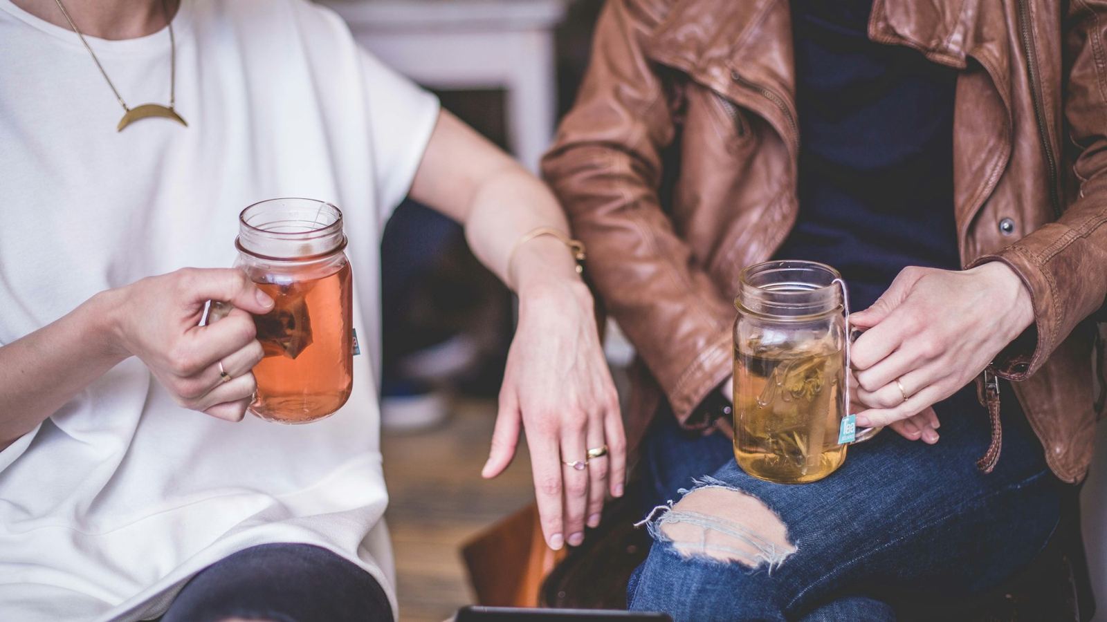 Two people sitting side by side, each holding a glass mug of tea